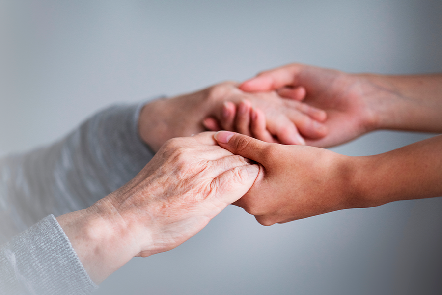 Mãos de uma pessoa idosa sendo seguradas pelas mãos de um cuidador, simbolizando empatia, cuidado e apoio. A imagem destaca a importância do toque e da conexão emocional no cuidado aos idosos.